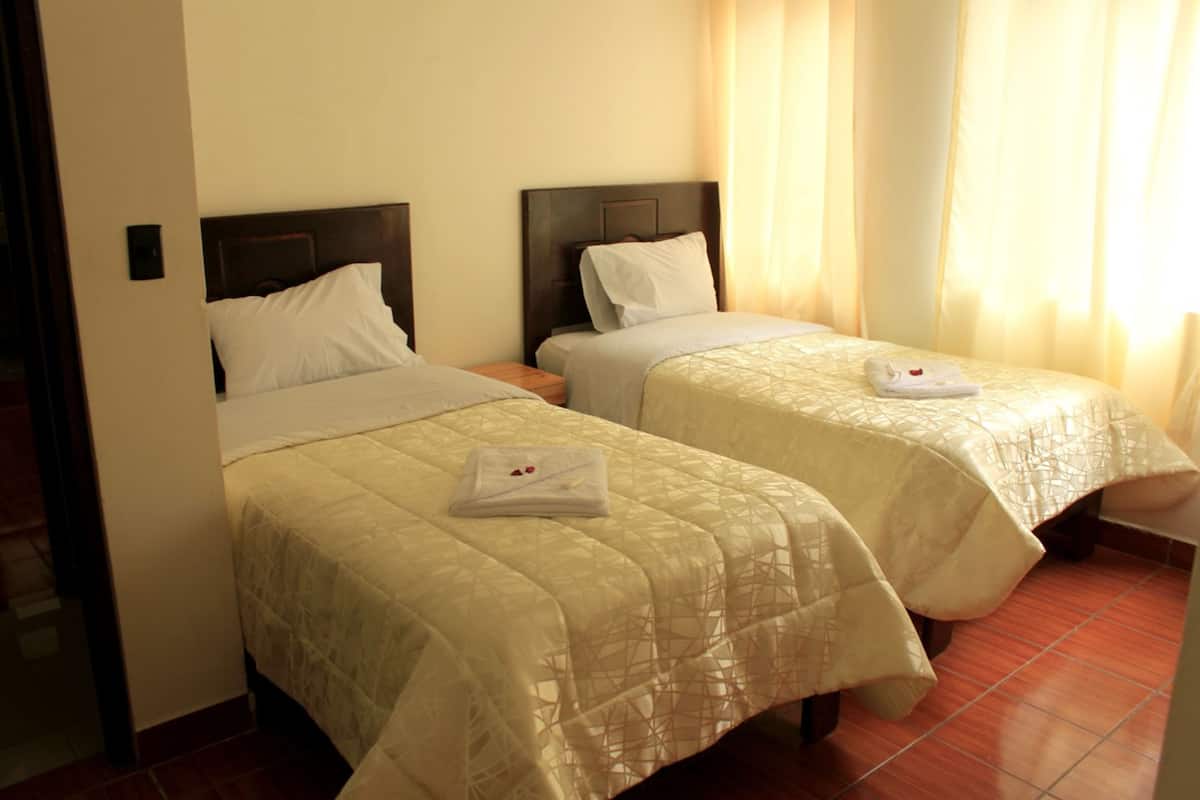 Quarto de hotel com duas camas, cada uma com colcha branca e toalha dobrada na cama.