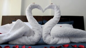 A bed with a blue bedspread and two white towels arranged in the shape of swans with red rose petals scattered around. - Casa Blanca Machu Picchu B&B (Machu Picchu)