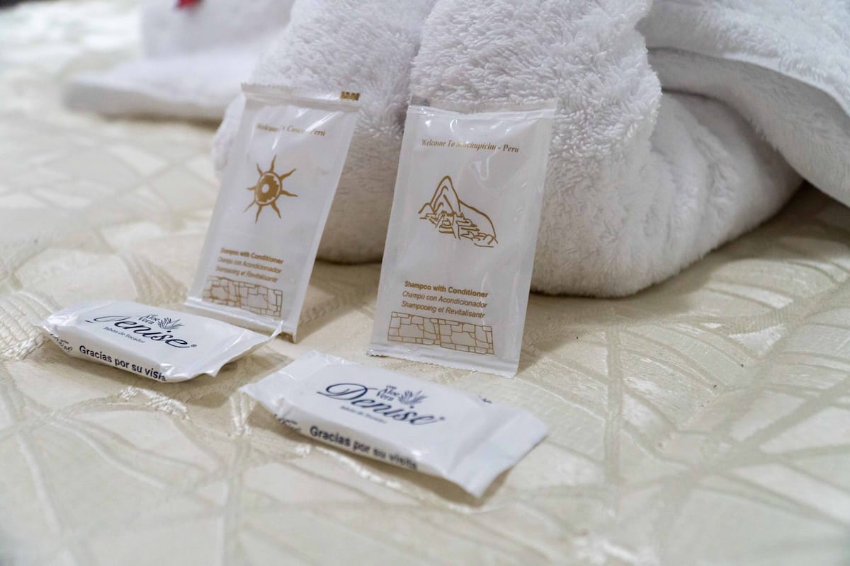 Artigos de higiene pessoal, incluindo shampoo e condicionador, sobre uma cama com toalhas brancas.