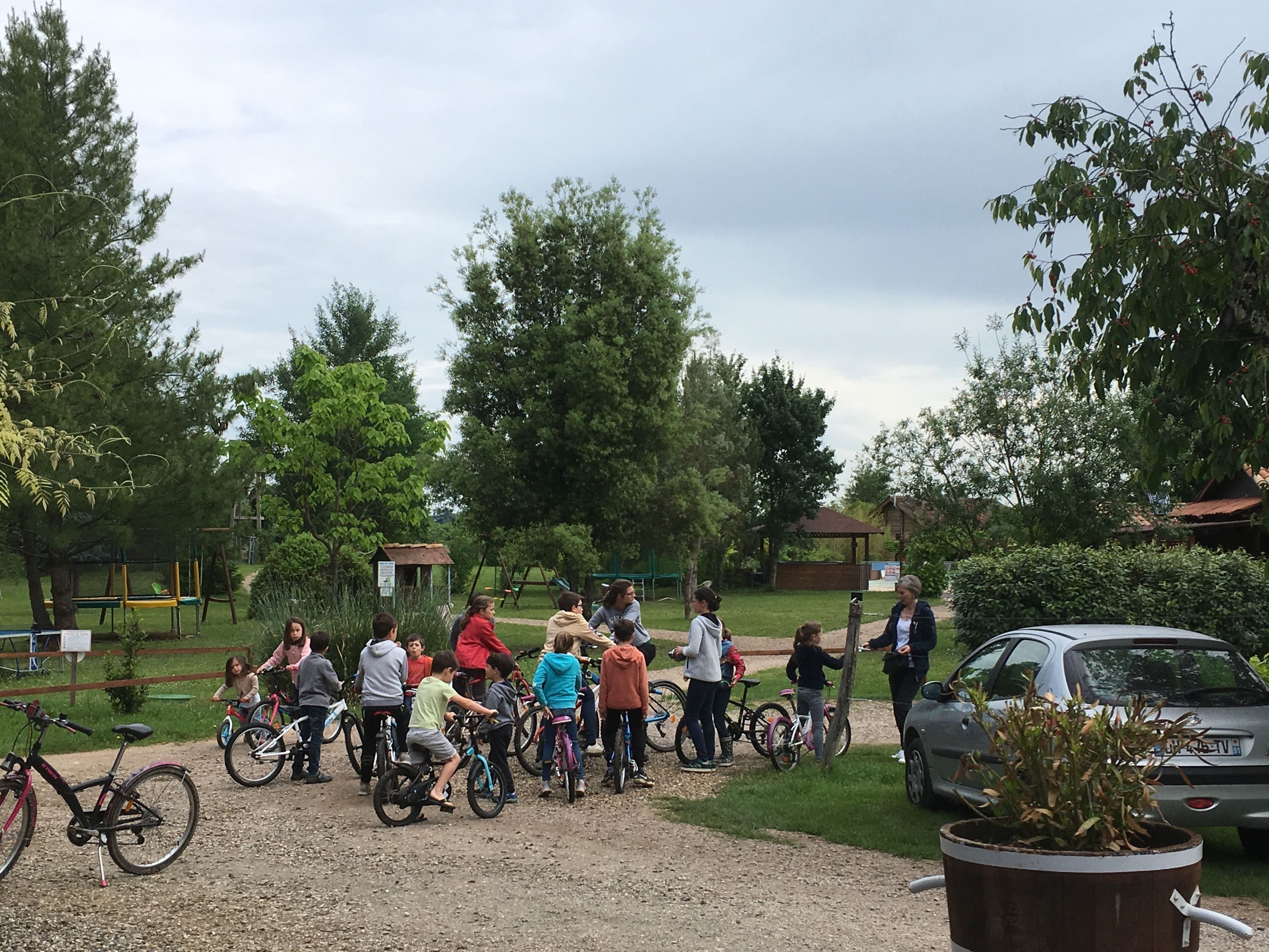 A group of people with bicycles in a park with trees and a playground.