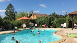 Une piscine où plusieurs personnes se baignent et profitent de l’eau, entourée de chaises longues et d’un espace abrité.