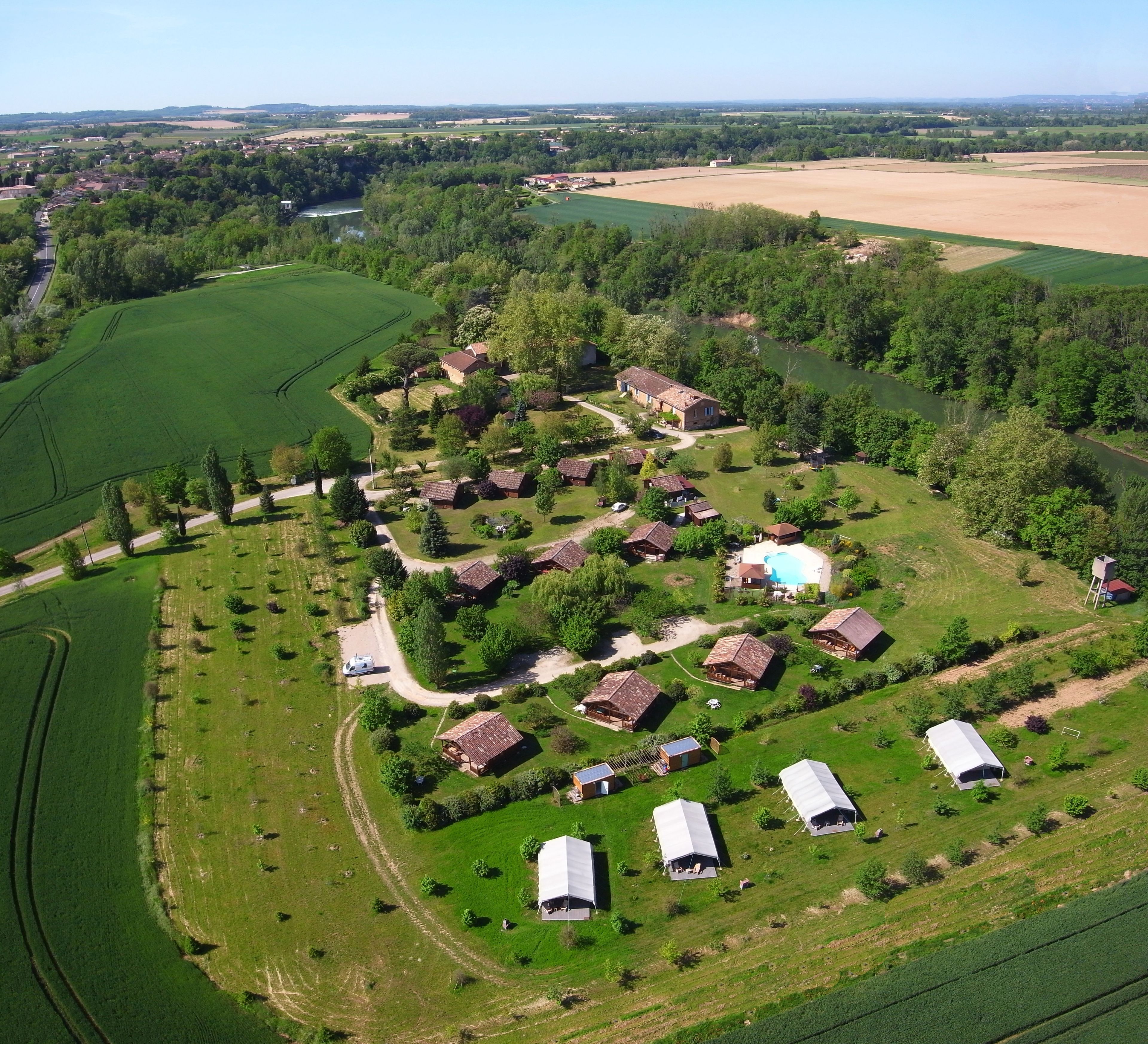 Vue aérienne d’une propriété rurale comprenant plusieurs bâtiments, une piscine et de vastes champs verdoyants.