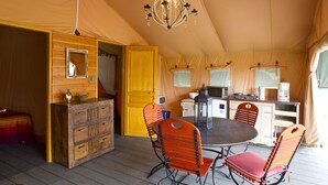 Un hébergement sous tente comprenant un espace repas, des meubles en bois et un lustre.