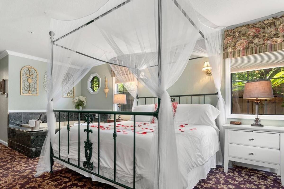 A four-poster canopy bed with a white canopy, a nightstand with a lamp, and a mirror above the bed.