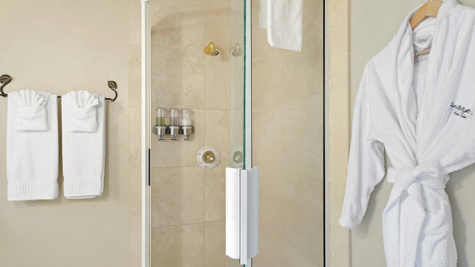 A bathroom with a glass shower door, two white towels on hooks, and a white bathrobe on a rack.