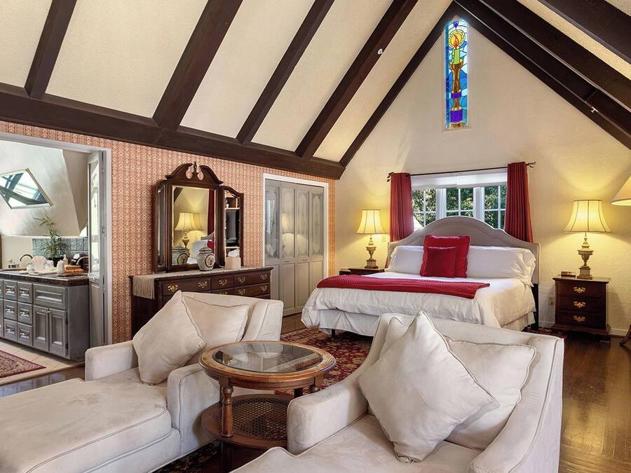 A spacious room with a large bed, a sitting area with a coffee table, and a view of the outdoors through a window.