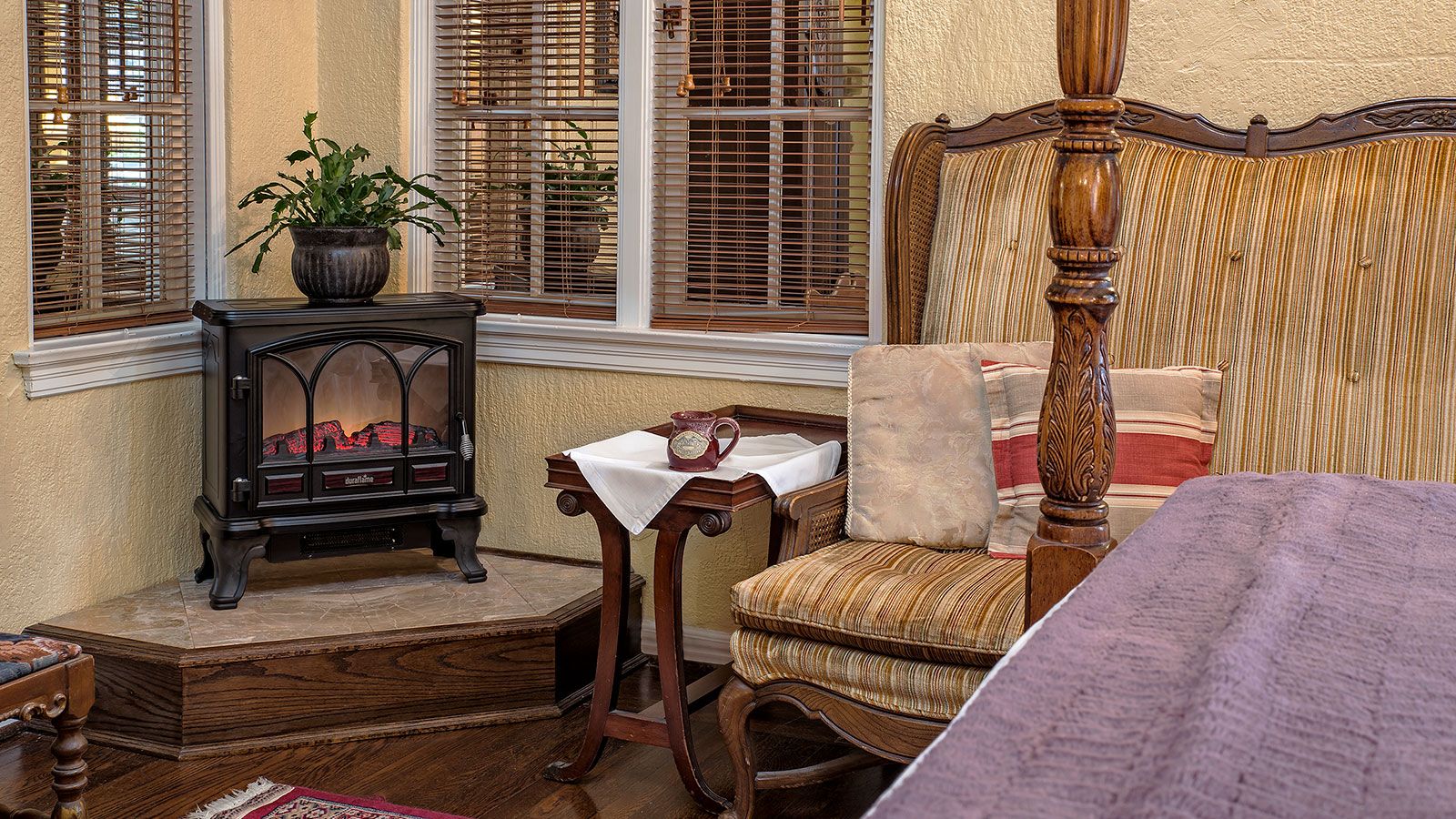 Una habitación con una cama con dosel, una mesa de madera con una jarra y una estufa.