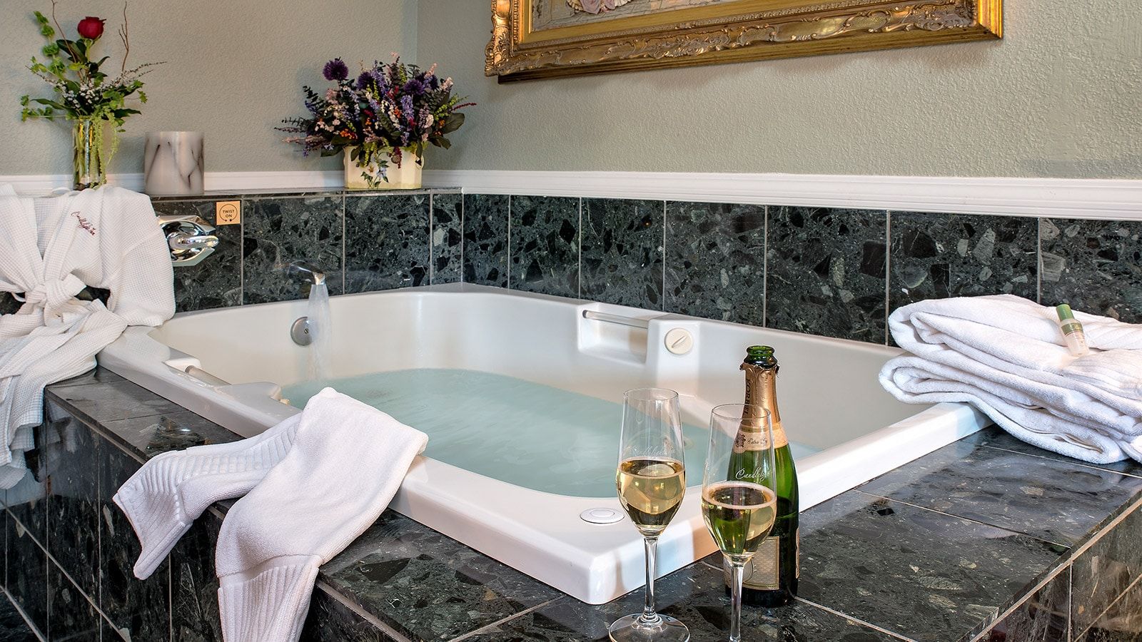 A bathroom with a bathtub, a bottle of champagne, and two glasses of wine.