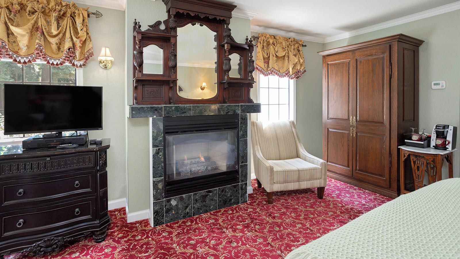 A room with a fireplace, a television, a wardrobe, and a chair.