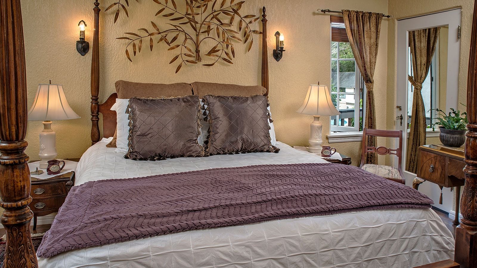 A bedroom with a bed, two bedside lamps, a decorative wall piece, and a window with curtains.