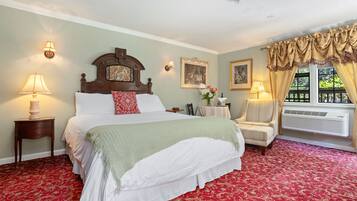 A hotel room with a large bed, two bedside tables with lamps, a chair, a small table with a vase, and a window with curtains.