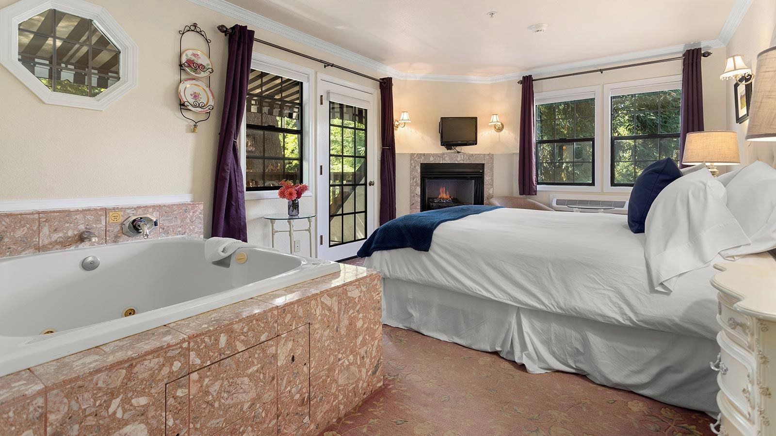 A bedroom with a large bathtub, a fireplace, and a bed with white bedding.
