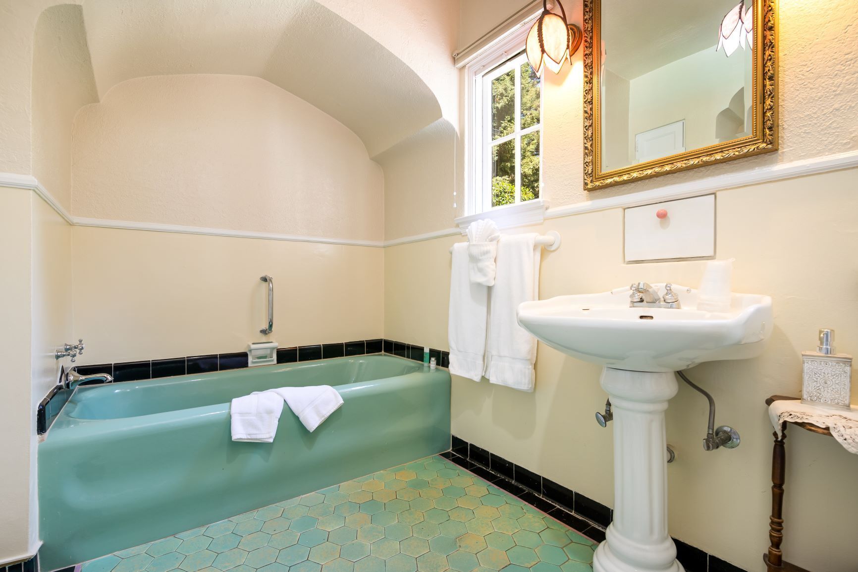 Un baño con una bañera verde, un lavabo blanco y un espejo grande con marco dorado.