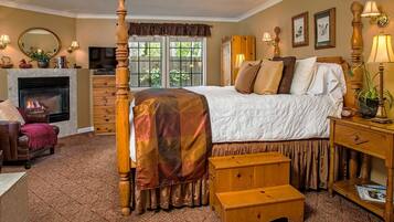 A bedroom with a four-poster bed, a fireplace, a television, and a window with a view of greenery.