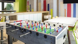 A modern indoor space with a foosball table, a large white table, and a colorful wall with vertical panels.
