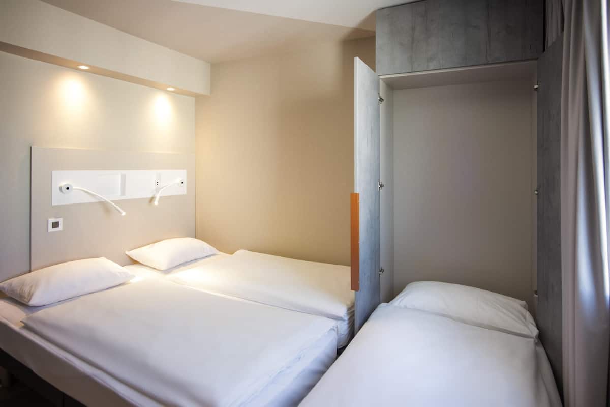 Une chambre d’hôtel avec deux lits simples, une tête de lit dotée d’un luminaire et une porte avec une poignée.