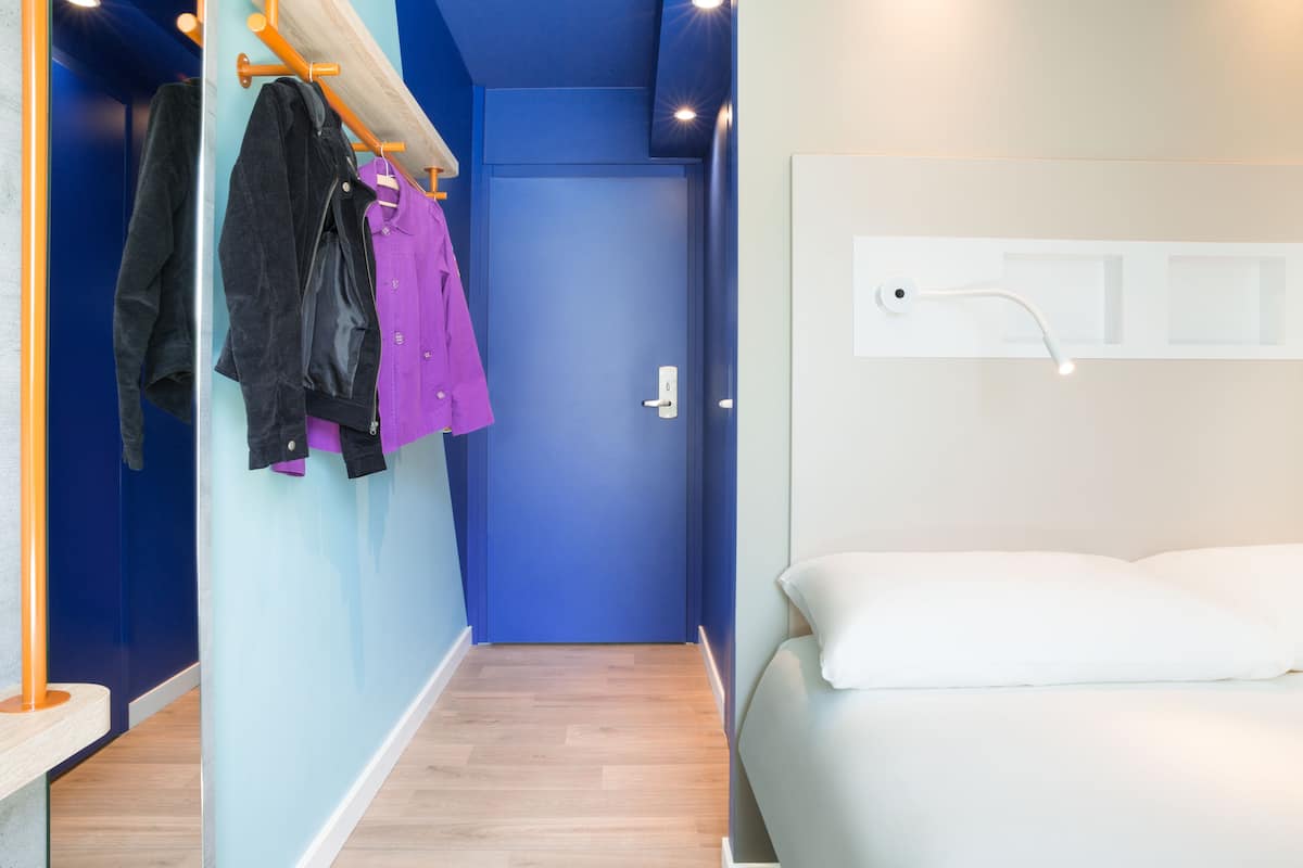 Une chambre d’hôtel avec une porte bleue, un lit avec du linge de lit blanc et un plancher en bois.