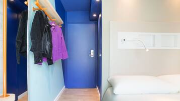 Una habitación de hotel con una puerta azul, una cama con ropa de cama blanca y suelo de madera.