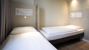 A hotel room with two single beds, a wooden headboard, a wall-mounted reading light, and a built-in shelf.
