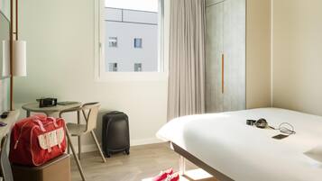 Een hotelkamer met een bed, een bureau, een stoel, een koffer, een rode tas en een paar schoenen.