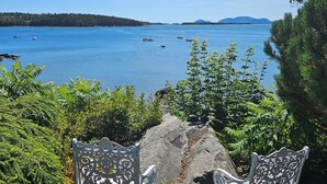 Two ornate metal chairs facing a body of water with boats, surrounded by greenery and a clear sky.