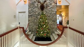 Un escalier avec un mur en pierre et une décoration représentant une tête de cerf, menant à un sapin de Noël.