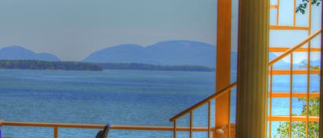 A wooden deck with a railing overlooking a body of water and distant mountains.