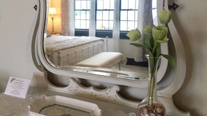 A mirror with a decorative frame, a bedside table with a lamp, a bed, and a vase with flowers.