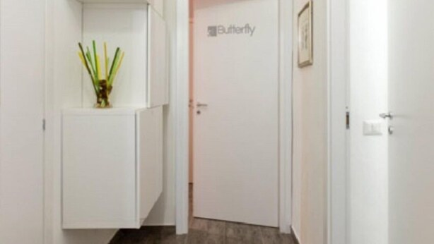 Un couloir aux murs blancs, une porte portant l’inscription « Papillon » et une petite plante posée sur un meuble.