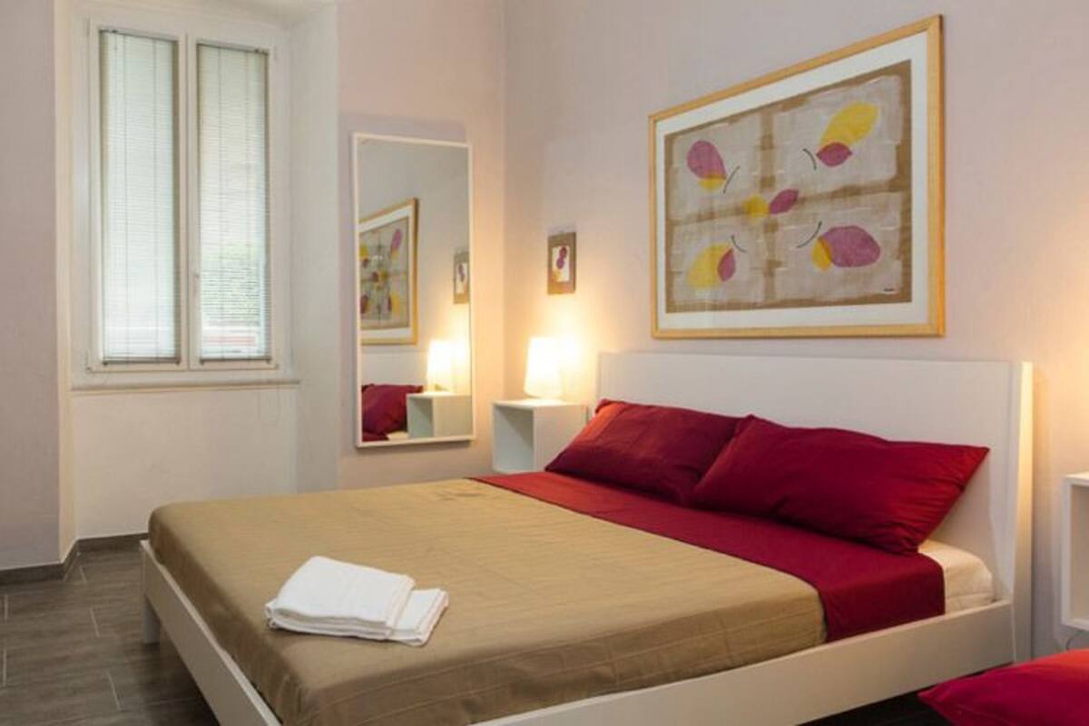 Habitación de hotel con cama, escritorio, silla, ventana y una obra de arte colgada en la pared.