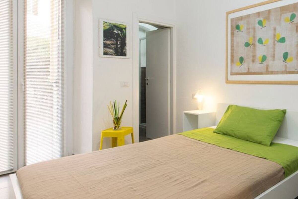 Un dormitorio con cama, mesita de noche, lámpara, silla y escritorio con computadora y teclado.
