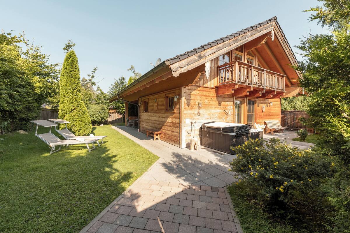 A log cabin with a balcony, a hot tub, and a patio area with sun loungers.