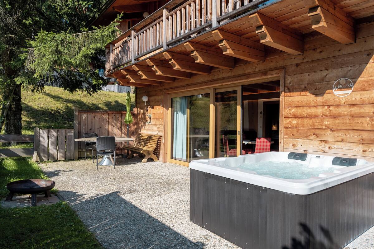 A wooden cabin with a hot tub, outdoor seating, and a balcony.