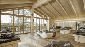 Een ruime kamer met grote ramen, houten vloeren en meerdere zithoeken, waaronder zitzakken en banken.