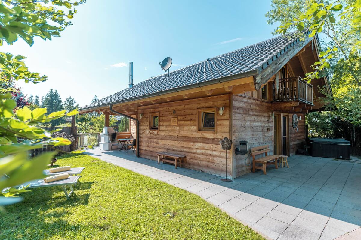 A wooden cabin with a balcony, a patio with a barbecue grill, and a small deck area.
