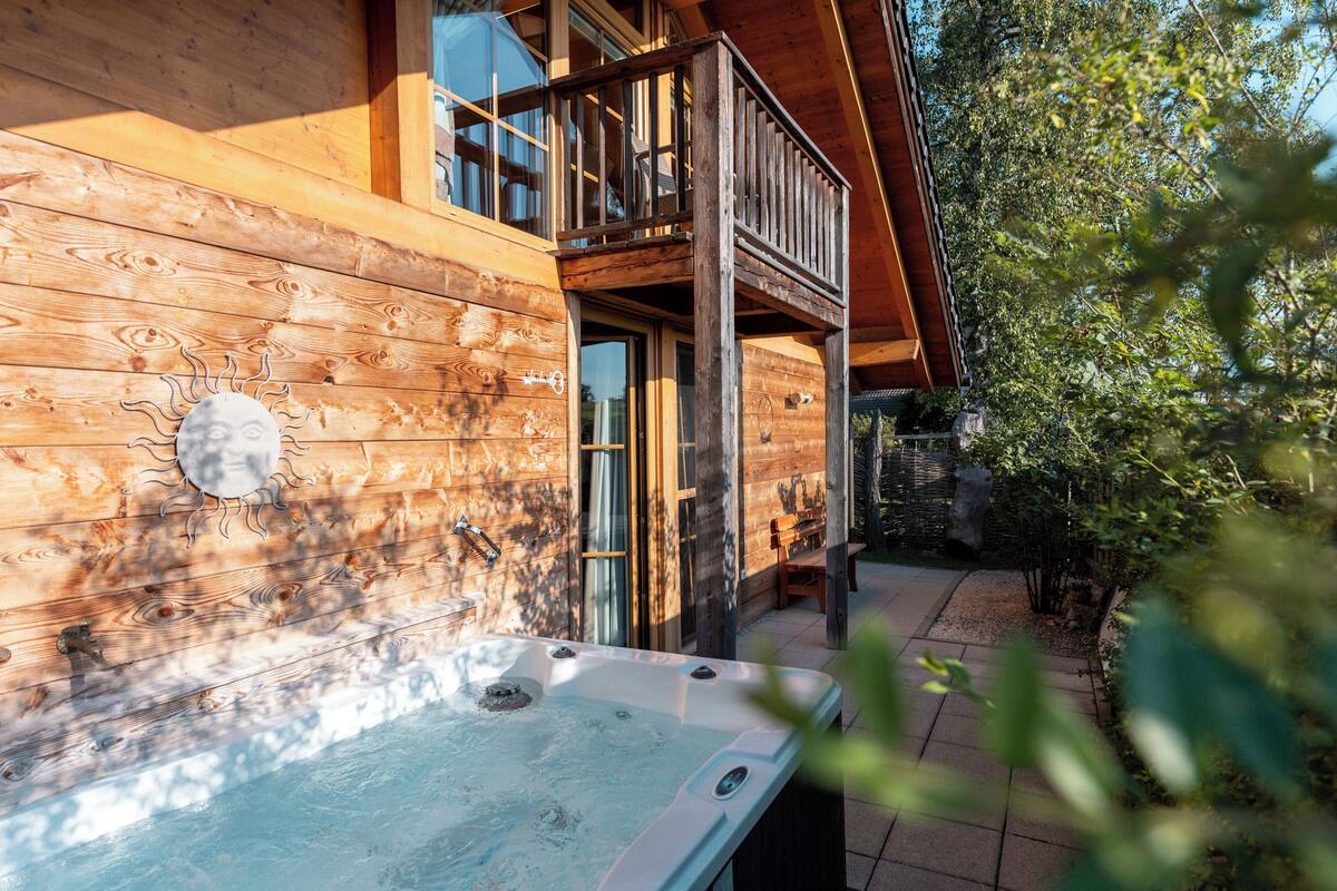 A wooden cabin with a hot tub, wooden deck, and a balcony.