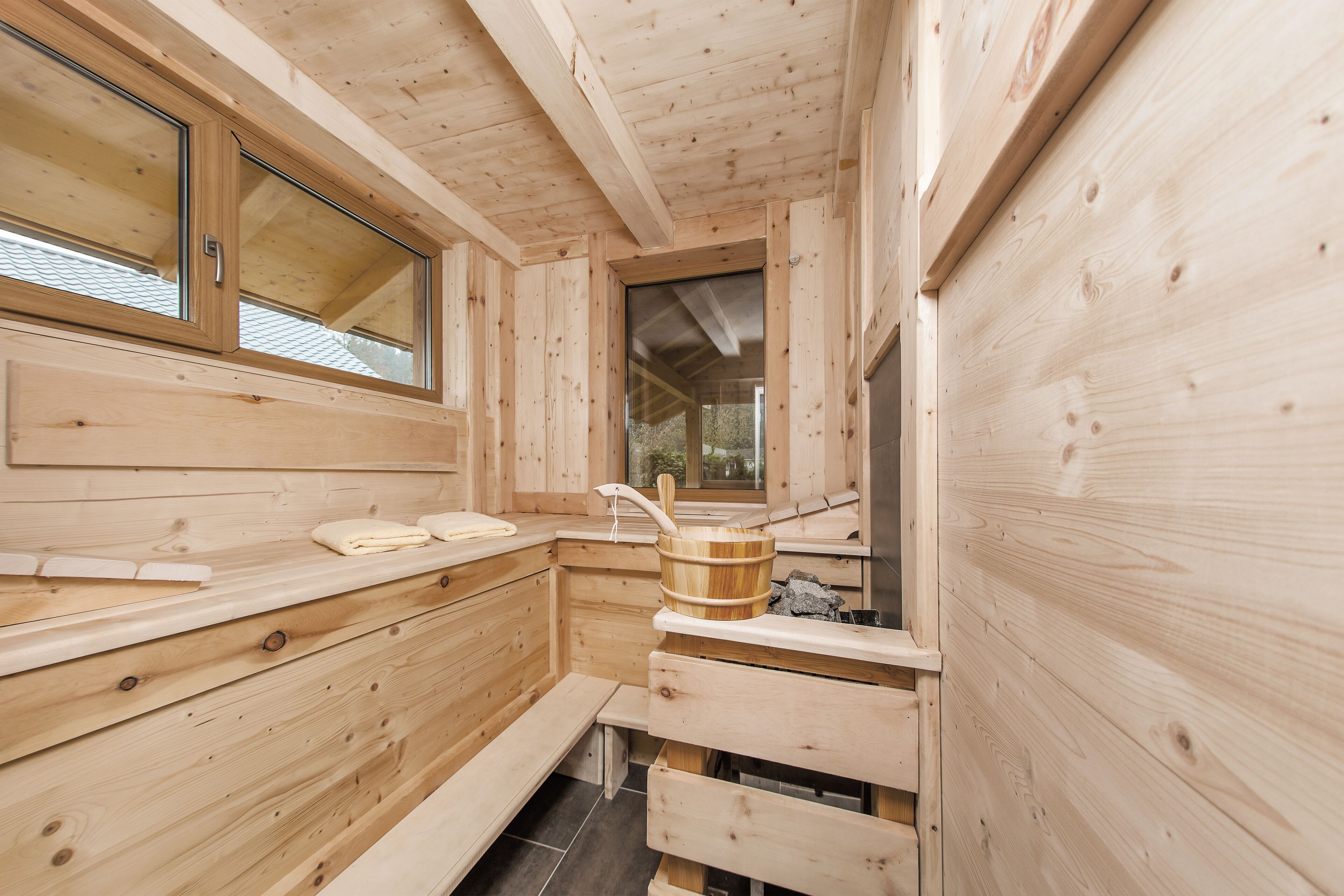 A wooden sauna room with benches, a wooden bucket, and a window.