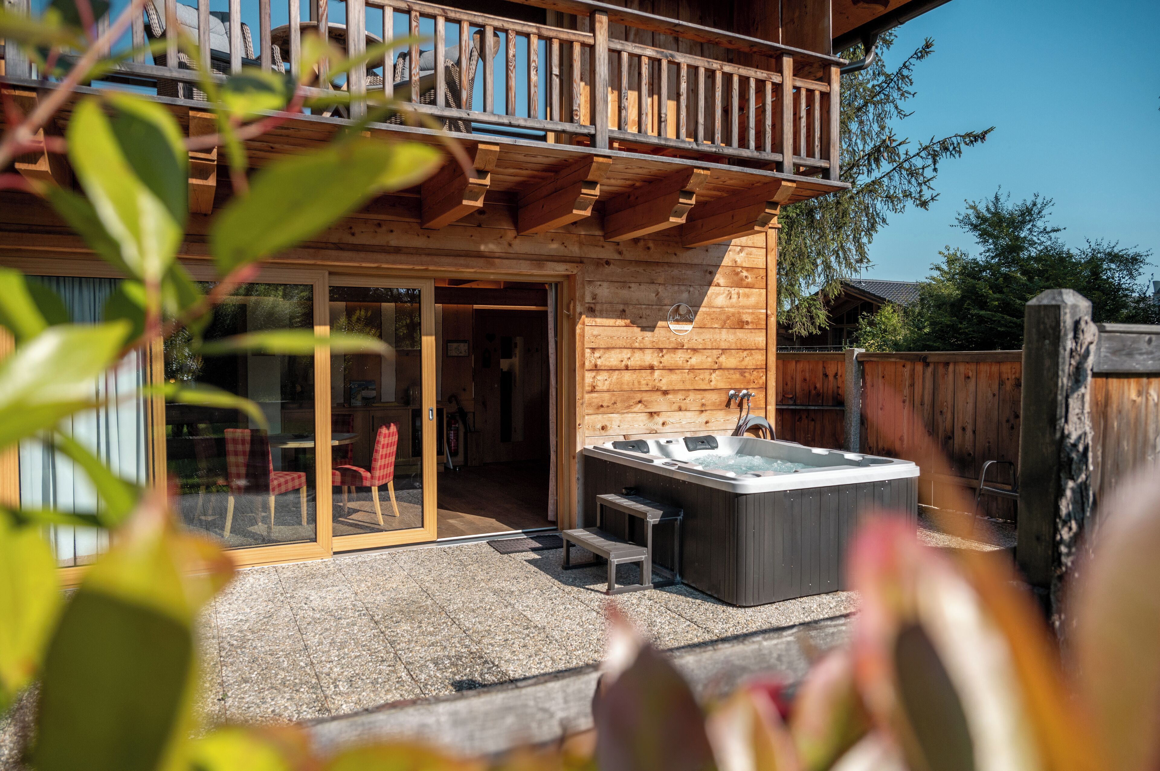 Una cabaña de madera con balcón, jacuzzi y un patio con sillas y una mesa.
