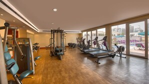 A spacious gym with various exercise equipment, large windows, and a view of the city.