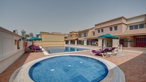 A swimming pool with lounge chairs and umbrellas, surrounded by buildings.