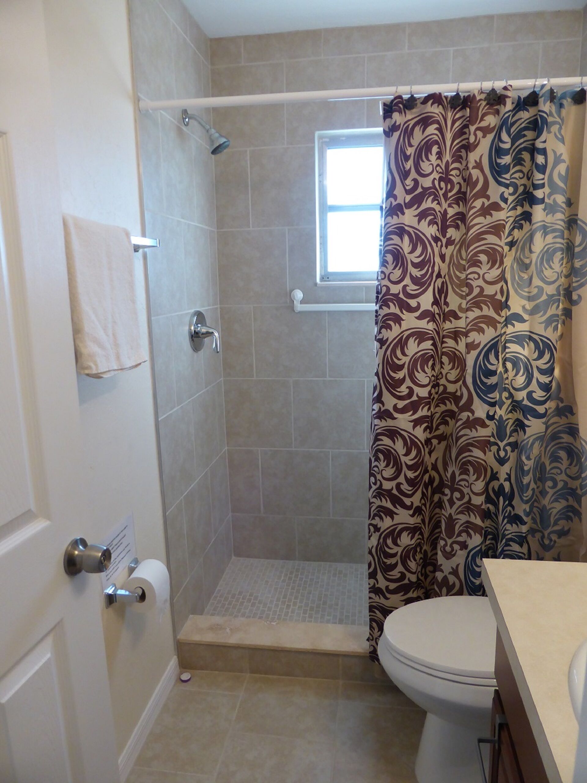 A bathroom with a shower, toilet, and a window.