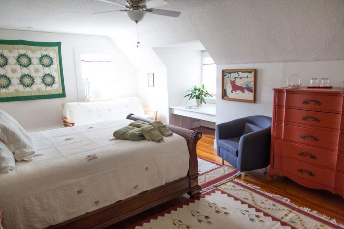 A bedroom with a bed, a dresser, a chair, and a ceiling fan.