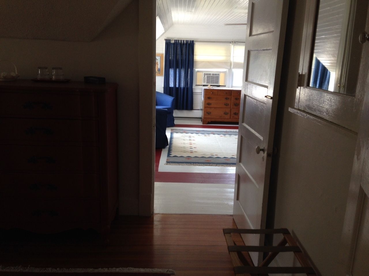 A room with a wooden dresser, a bed with a blue bedspread, and a window with curtains.