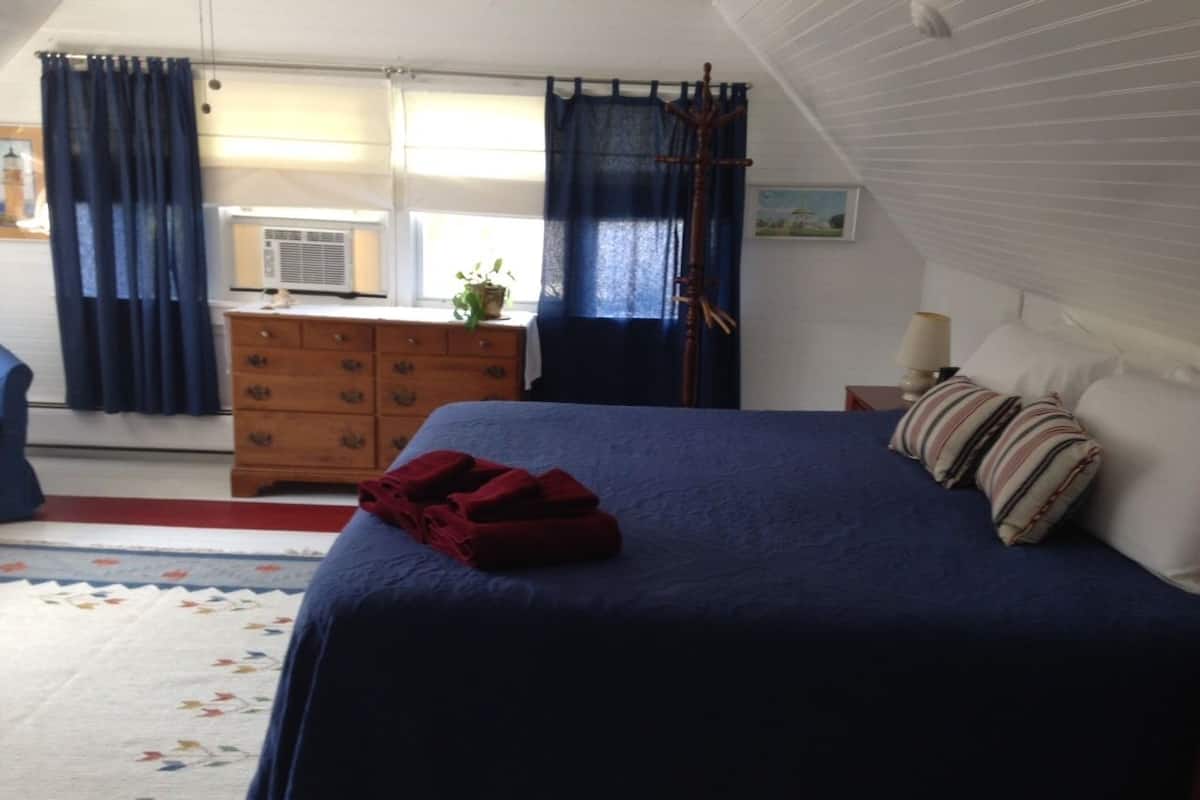 A bedroom with a bed, a dresser, a lamp, and a window with curtains.