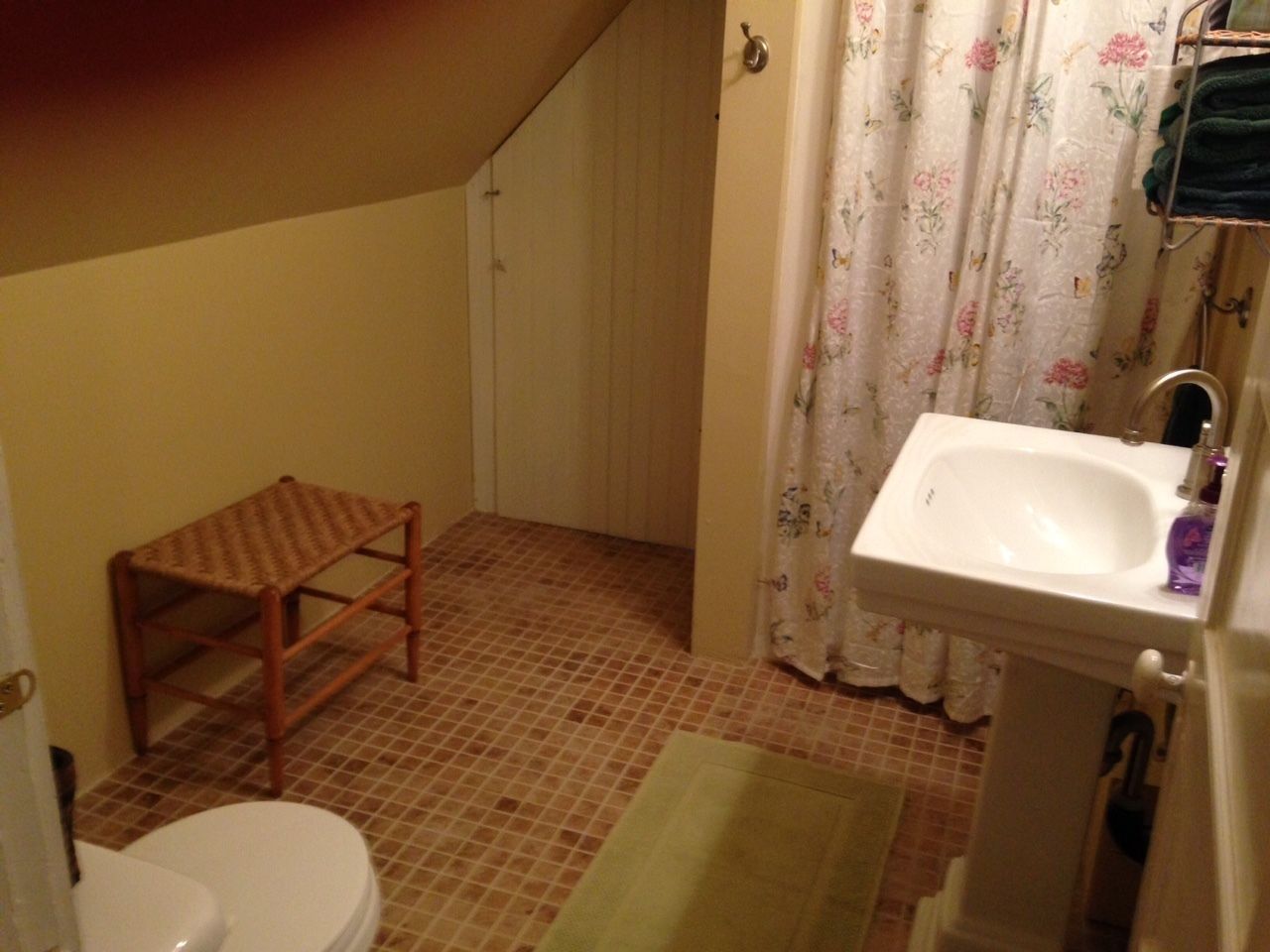 A small bathroom with a toilet, a wooden stool, a sink, and a shower curtain.