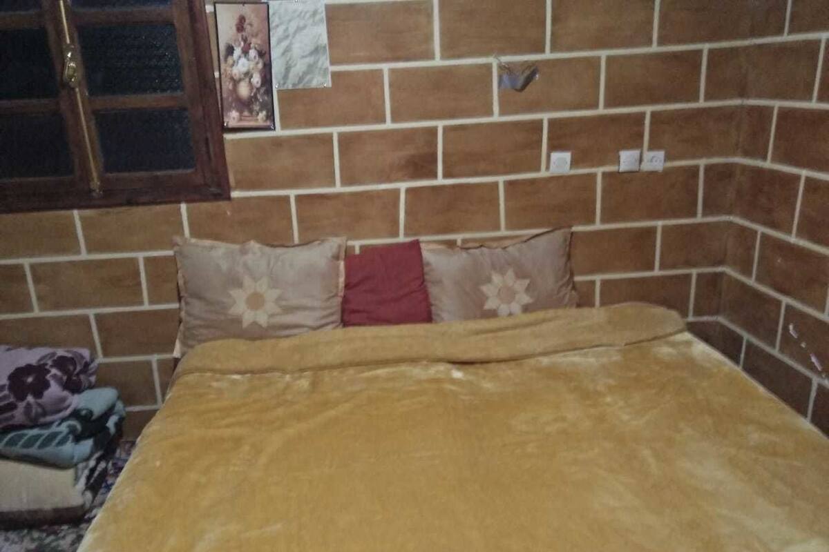 A room with a brick-patterned wall, a bed with a brown blanket, and a window with a wooden frame.