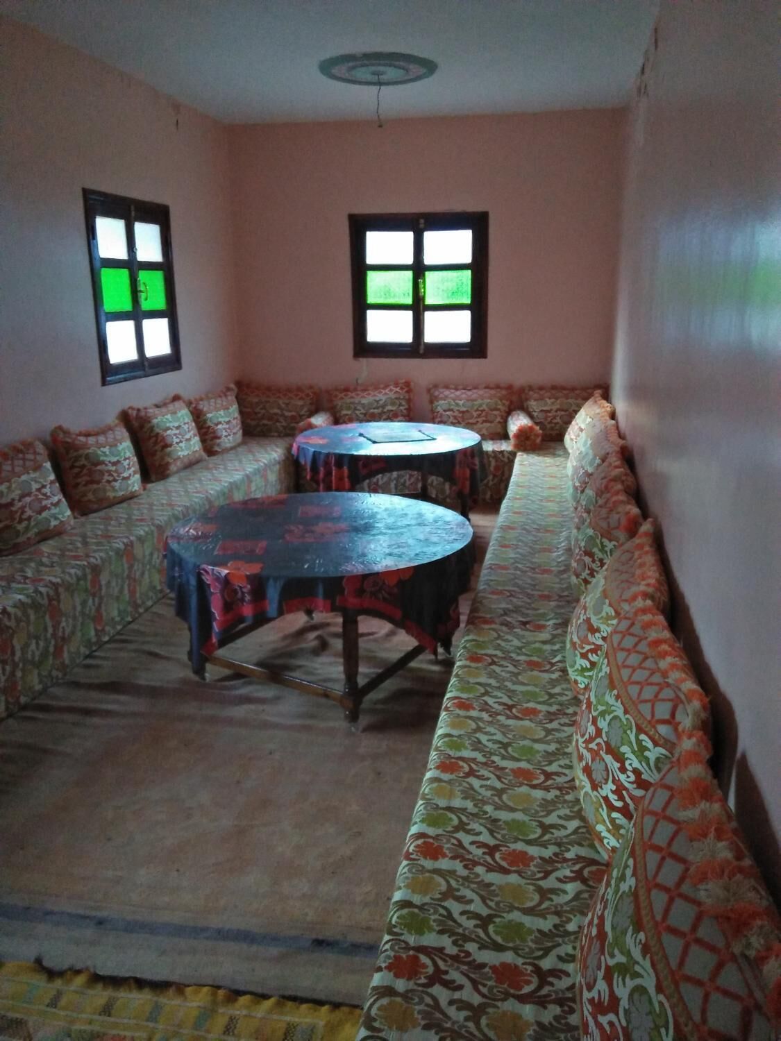 A room with a long sofa, a round table, and two windows with green-tinted glass.