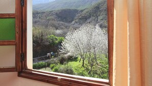 Una ventana con vista a un paisaje montañoso, cielo despejado y una persona caminando por un sendero.