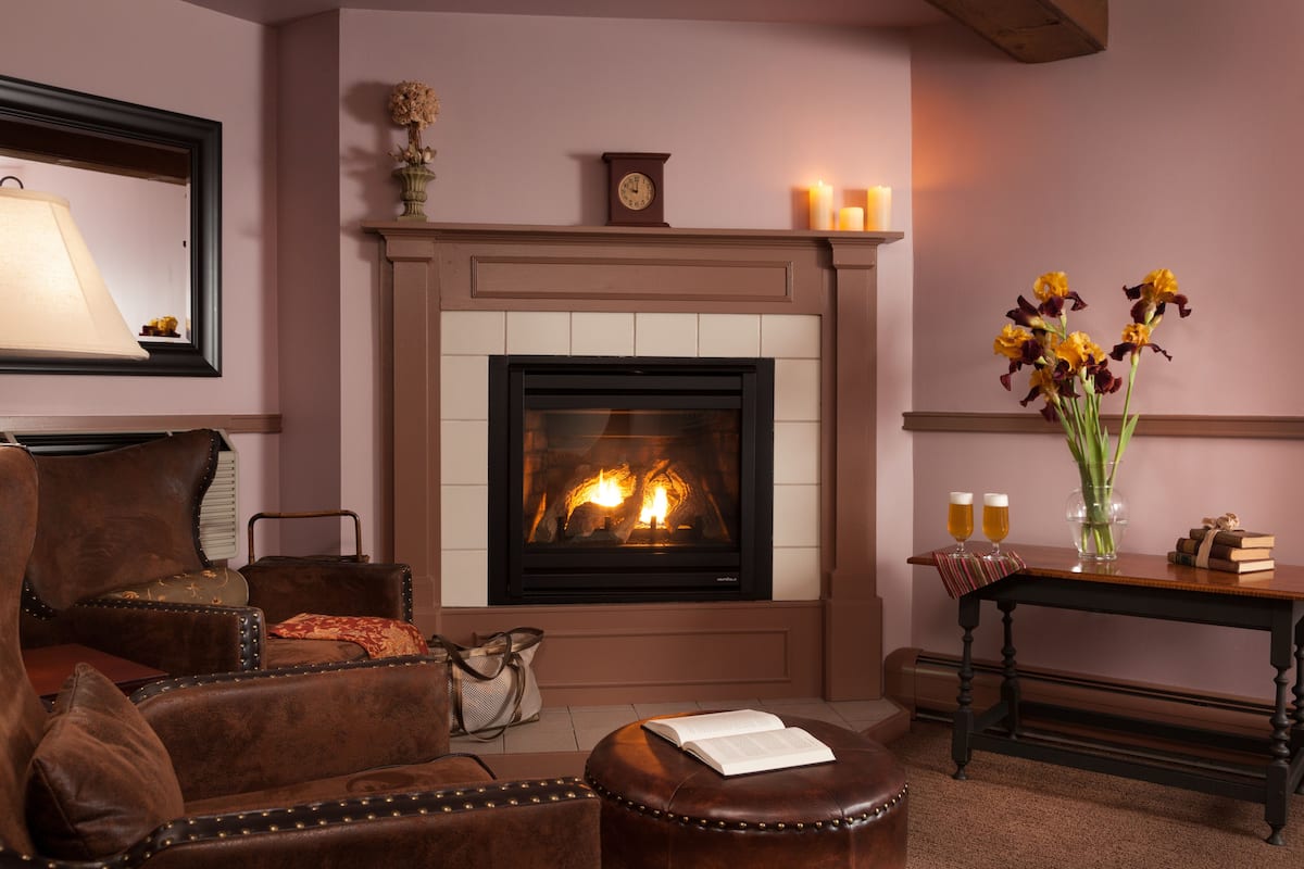 A cozy living room with a fireplace, leather armchairs, a coffee table with a book, and a vase with flowers.