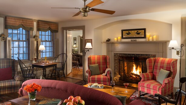 A cozy living room with a fireplace, plaid armchairs, a sofa, and a dining area with a chessboard. - Rabbit Hill Inn (Lower Waterford)